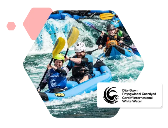 Paddlers in inflatable kayaks on the rapids at Cardiff International White Water, beside the centre’s logo