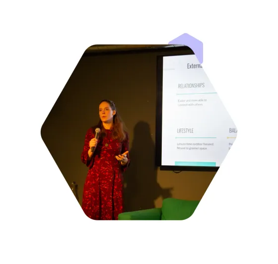A speaker on stage with a microphone, beside a slide setting out relationships, lifestyle and balance